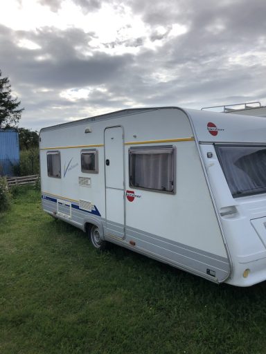 Wohnwagen Bürstner von rechts, weiß mit Streifen in blau und gelb, teilbare Eingangstür