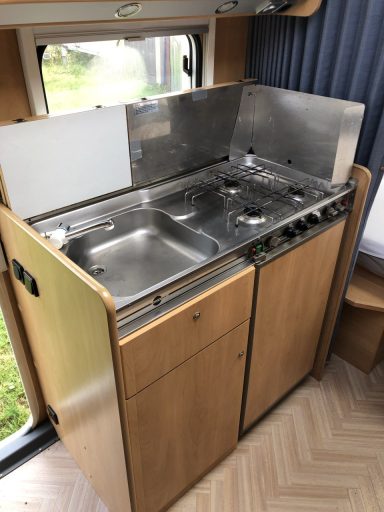 Küche im Wagen. Rechts Spüle mit Wasserhahn dann 3 flammiger Gaskocher. Darunter der Kühlschrank und Stauraum.