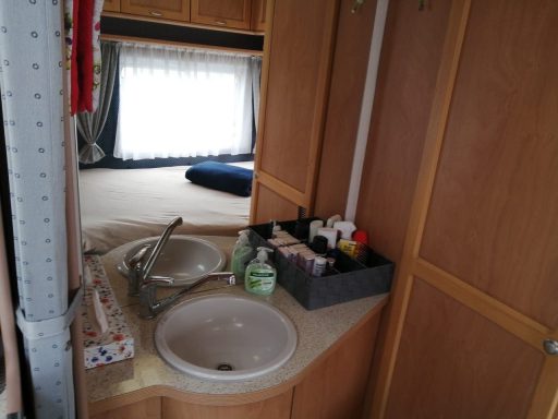 In der Mitte rundes Waschbecken, dahinter große Spiegelrückwand, links Vorhang rechts Tür zu WC