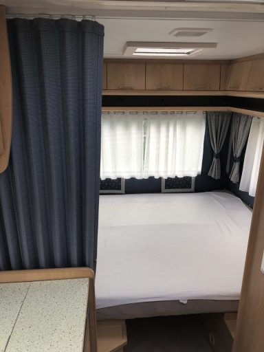 Doppelbett mit Matratzenschoner, Fenster und Vorhang.